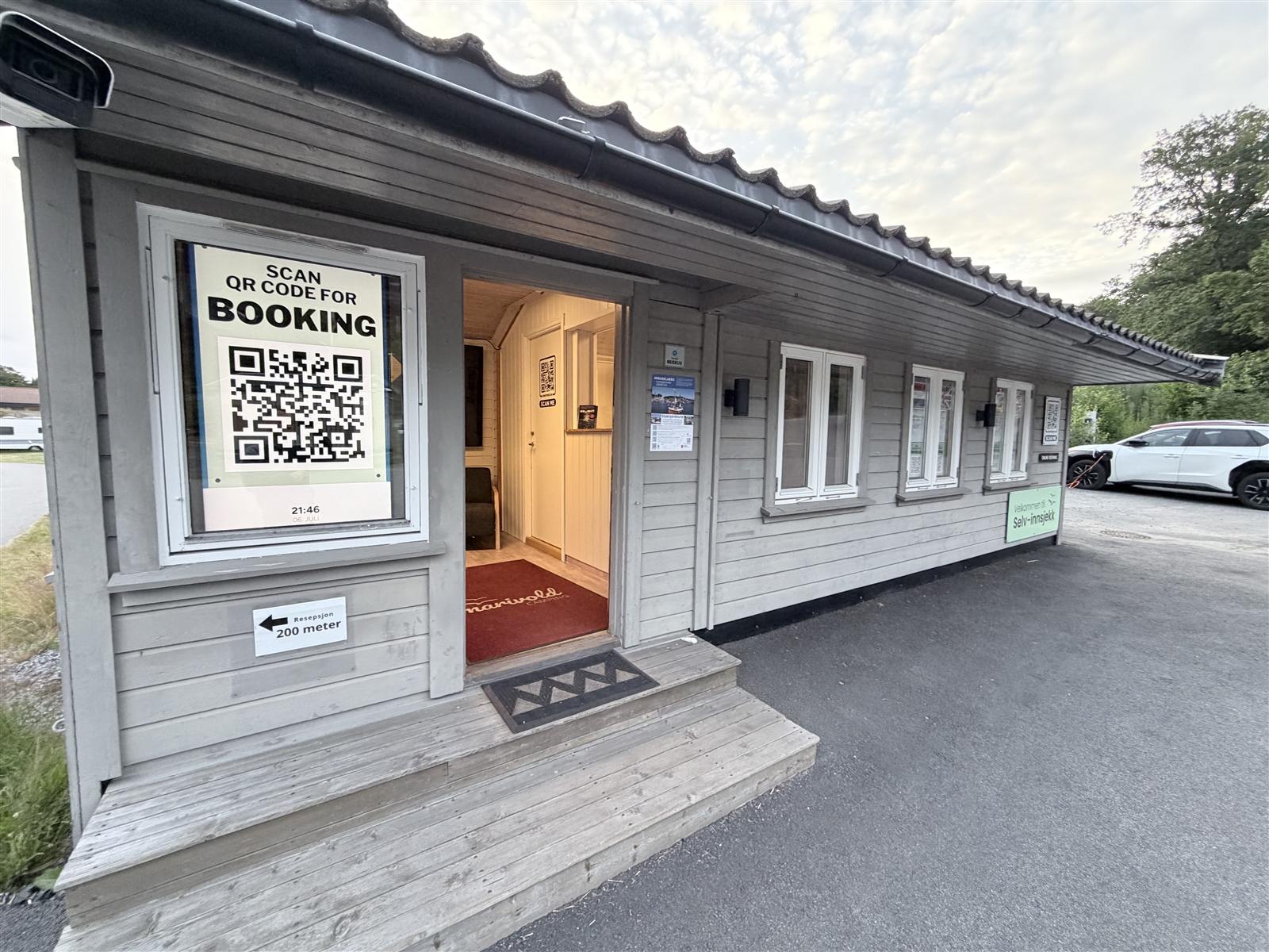 Inngangen til selvinnsjekk-bua med QR-kode for booking og skilt mot resepsjonen